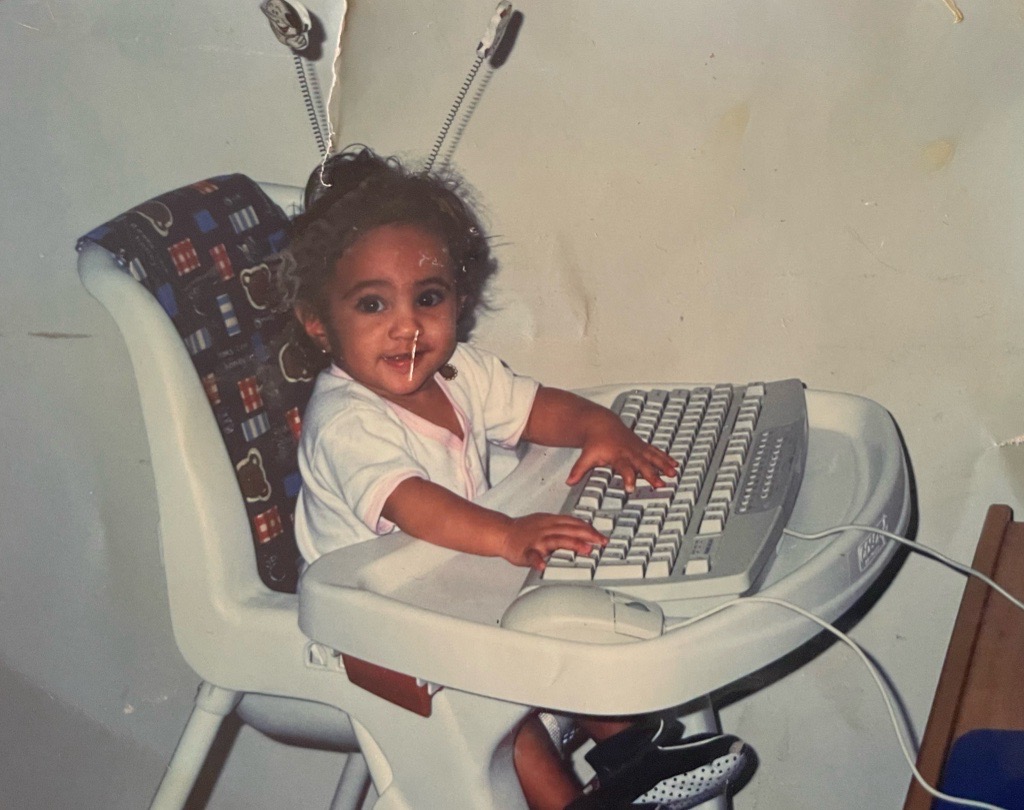 A childhood photo of Rana sat typing at a computer (2).